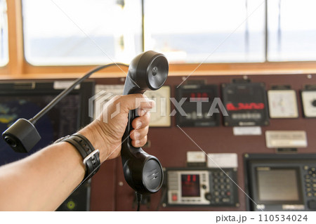 Navigational control panel and VHF radio with hand. Radio communication at sea. Working on the ship's bridge. Navigational control panel and VHF radio with hand. Radio communication at sea. Working on the ship's bridge. 110534024