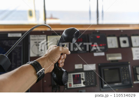 Navigational control panel and VHF radio with hand. Radio communication at sea. Working on the ship's bridge. 110534029