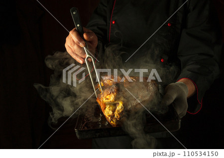 Cooking a rooster carcass on a baking sheet. Black space for recipe or menu. Baked chicken and fork in the hands of a chef 110534150