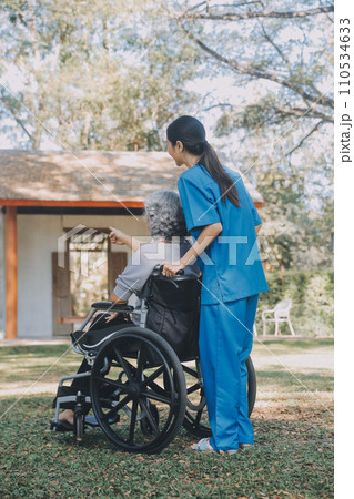 Young asian care helper with asia elderly woman on wheelchair relax together park outdoors to help and encourage and rest your mind with green nature. Help support yourself to learn to walk. walker 110534633