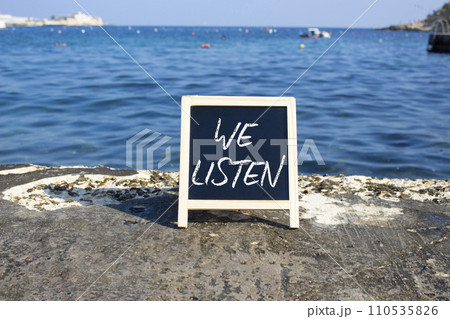 We listen symbol. Concept words We listen on black chalk background. Beautiful sea background. Business and We listen concept. Copy space. 110535826