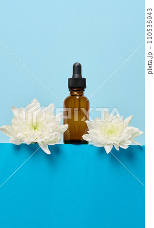A glass brown bottle with a dropper on a blue background, a container for cosmetic products. A glass brown bottle with a dropper on a blue background, a container for cosmetic products. 110536943