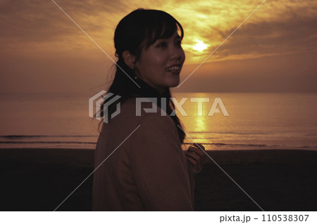 冬の海で夕焼けを楽しむ若い女性 冬の海で夕焼けを楽しむ若い女性 110538307