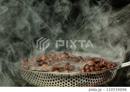 Roasted Coffee seeds with smoke. Beans Coffee roasted on pile and hot smoke raise up in line shape. Roasted coffee bean create scent aroma. Black background isolated 110539896