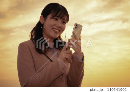夕焼けの中でスマホを使う女性 110541902