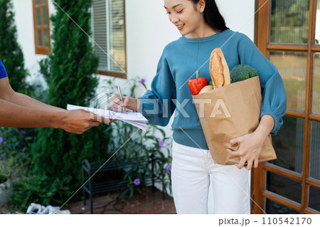 Asian woman signing the receipt on the order receipt through the online supermarket's home store Asian woman signing the receipt on the order receipt through the online supermarket's home store 110542170