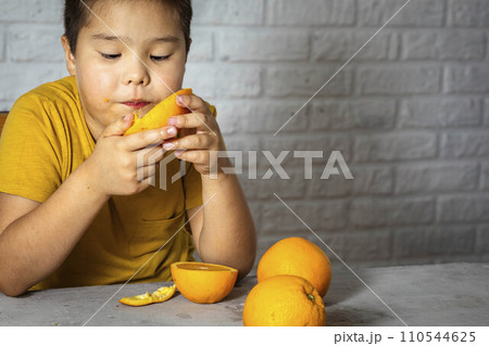 A curious Asian boy in a yellow T-shirt enjoys a juicy orange, the concept and benefits of vitamin C 110544625