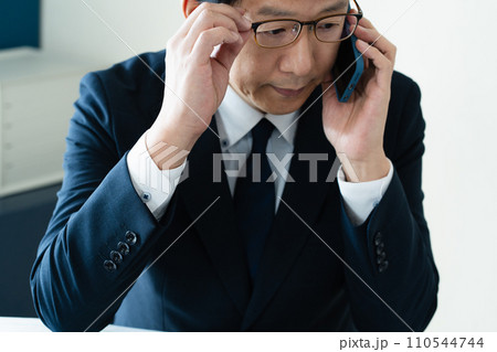 パソコンを見ながらスマホで通話するビジネスマン 110544744