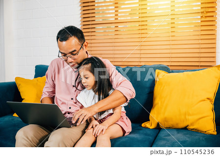 In a modern living room an Asian businessman combines work with family as his daughter uses a computer for e-learning. Their bonding and happiness showcase the essence of togetherness. In a modern living room an Asian businessman combines work with family as his daughter uses a computer for e-learning. Their bonding and happiness showcase the essence of togetherness. 110545236