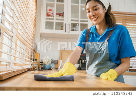 Maid with protective glove cleans wood dining table in cozy kitchen. professional cleaning products for perfect home tidiness. Cleaner working safety glove hygiene routine. Maid housekeeping concept. Maid with protective glove cleans wood dining table in cozy kitchen. professional cleaning products for perfect home tidiness. Cleaner working safety glove hygiene routine. Maid housekeeping concept. 110545242
