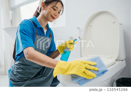 Dedicated maid in rubber gloves scrubs toilet seat with cloth ensuring hygiene in the bathroom. Her focus on cleanliness highlights the essence of housekeeping. Housekeeper healthcare concept Dedicated maid in rubber gloves scrubs toilet seat with cloth ensuring hygiene in the bathroom. Her focus on cleanliness highlights the essence of housekeeping. Housekeeper healthcare concept 110545266