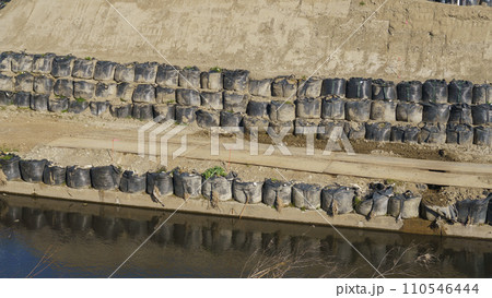 水害で河川沿いに設置された大型土のう 110546444