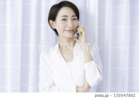 リビングでスマホ通話するミドルの女性 110547802