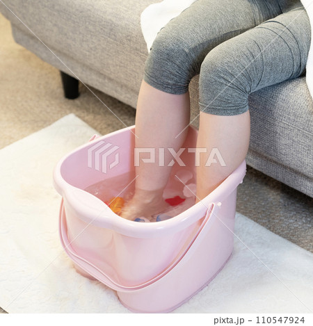 ソファーに座って足湯を使う女性の足元 110547924
