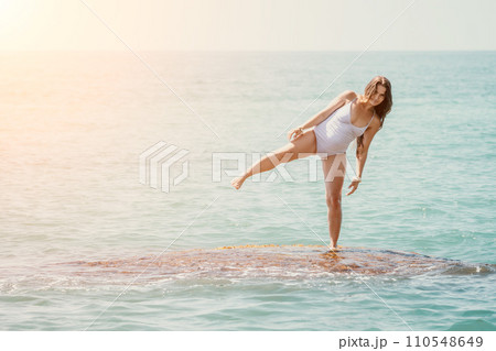 Woman sea yoga. Back view of free calm happy satisfied woman with long hair standing on top rock with yoga position against of sky by the sea. Healthy lifestyle outdoors in nature, fitness concept Woman sea yoga. Back view of free calm happy satisfied woman with long hair standing on top rock with yoga position against of sky by the sea. Healthy lifestyle outdoors in nature, fitness concept 110548649