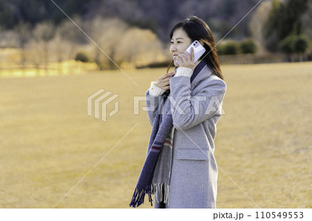 冬の公園でスマホ通話する女性 110549553