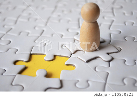 Wooden doll on top of jigsaw with missing jigsaw puzzle. Hiring and employment concept Wooden doll on top of jigsaw with missing jigsaw puzzle. Hiring and employment concept 110550223