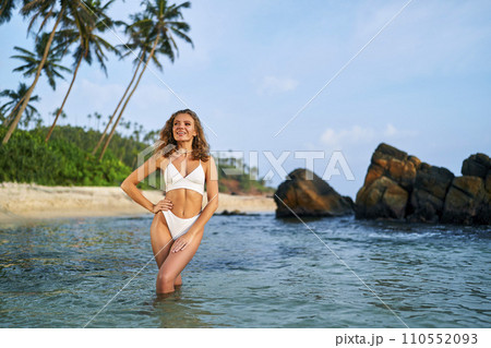 Fit woman enjoys sunbathing in bikini on tropical beach. Slender female applies sunscreen for safe tan. Health-conscious sunbather on seaside vacation. Tanned lady proactive in skin protection. Fit woman enjoys sunbathing in bikini on tropical beach. Slender female applies sunscreen for safe tan. Health-conscious sunbather on seaside vacation. Tanned lady proactive in skin protection. 110552093