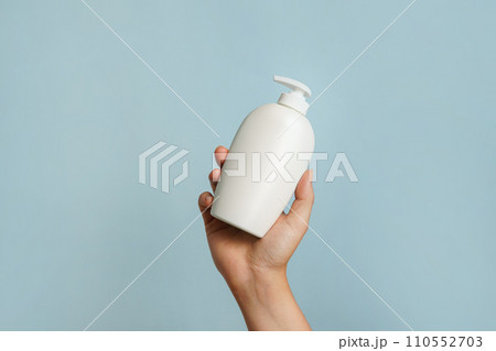 Woman holding white bottle of lotion, soap or shampoo in her hand, blue background 110552703