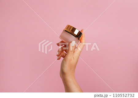 Female hand holding golden jar of cosmetic cream on pink background. Cosmetic beauty product branding mockup. Copy space Female hand holding golden jar of cosmetic cream on pink background. Cosmetic beauty product branding mockup. Copy space 110552732