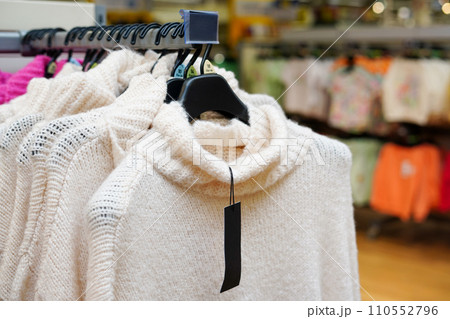 Stylish clothes on hangers in the store, white sweaters 110552796