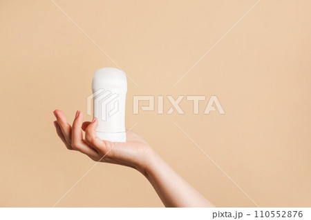 Female hand holds white body deodorant on beige background, copy space 110552876