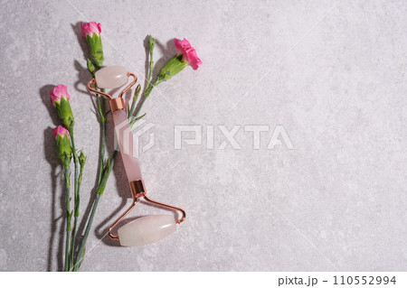 Facial jade massage gua sha roller with trendy shadows and flowers on concrete background, beauty anti aging tools Facial jade massage gua sha roller with trendy shadows and flowers on concrete background, beauty anti aging tools 110552994