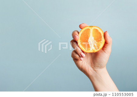 Female hand holding orange on blue background, copy space 110553005