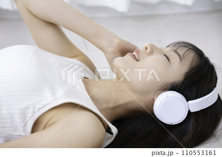 フローリングに寝転んで音楽に浸る女性 110553161