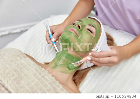 female beautician applies the mask to the face of beautiful woman in the spa salon. facial skin care female beautician applies the mask to the face of beautiful woman in the spa salon. facial skin care 110554834