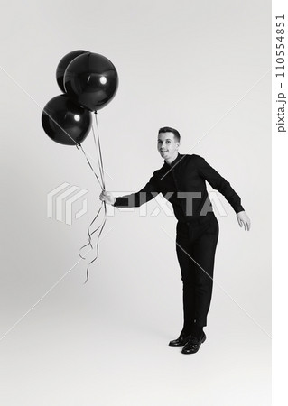 elegant caucasian man with bunch of black air balloons on white background. black and white 110554851