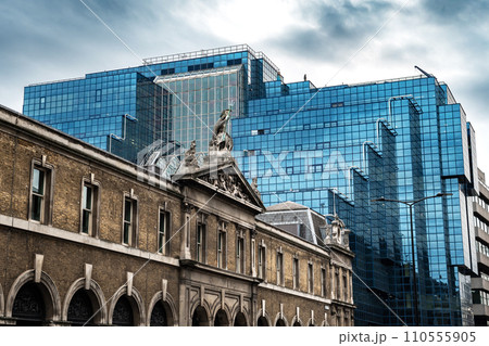 Old Historic Building In Front Of Modern Office Building With Blue Glass Facade In The Finance District Of London, United Kingdom 110555905