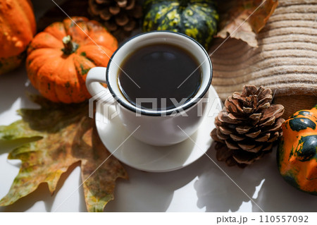 Autumn, fall leaves, hot steaming cup of coffee and a warm scarf on white table background. Seasonal, morning coffee, Sunday relaxing and still life concept 110557092