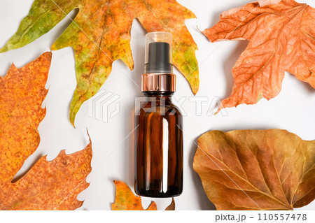 Brown cosmetic dropper bottle with dry falling leaves on grey background. Autumn composition. Concept of natural and organic skincare products 110557478
