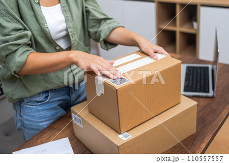 Seamlessly connected: Woman's hands apply a QR code sticker to a package, showcasing the essence of online shopping and e-commerce delivery. Seamlessly connected: Woman's hands apply a QR code sticker to a package, showcasing the essence of online shopping and e-commerce delivery. 110557557
