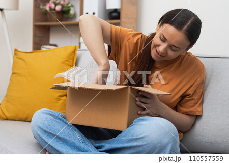 Brunette woman consumer takes out clothes from open cardboard box in premise of apartment concept of online shopping and delivery of parcels with goods to home Brunette woman consumer takes out clothes from open cardboard box in premise of apartment concept of online shopping and delivery of parcels with goods to home 110557559
