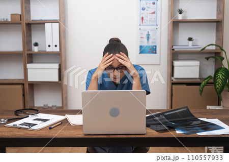 Pensive female doctor works at laptop resting head on hands tiredly exhausted young practitioner solves complex problems regarding patient treatment sitting in office 110557933