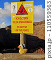 Warning sign with a Yellow knitted duck with a woolen hat on a wooden bench on the background of the volcano 110559363