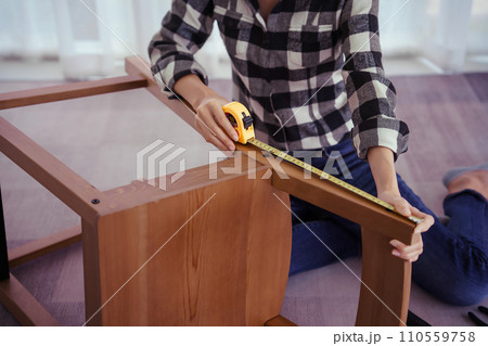 Women measuring length of chair with measure tape while assembling and renovation chair furniture Women measuring length of chair with measure tape while assembling and renovation chair furniture 110559758