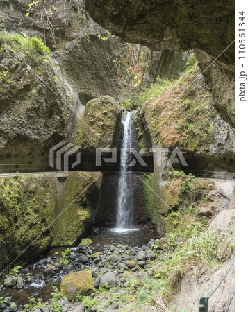 View of waterfall crossing the path at levada, water irrigation channel and tropical plants at hiking trail Levada do moinho to levada nova waterfall. Madeira, Portugal 110561344