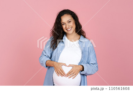 Positive expecting young woman holding hands on tummy Positive expecting young woman holding hands on tummy 110561608