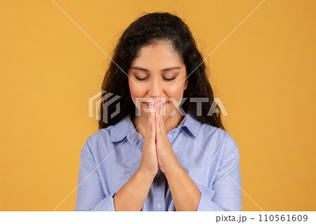 Contemplative young woman with eyes closed and hands pressed together in a prayerful Contemplative young woman with eyes closed and hands pressed together in a prayerful 110561609