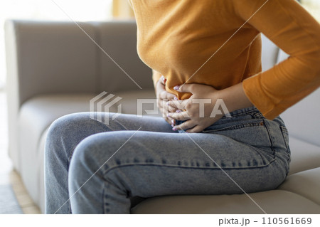 Unrecognizable woman experiencing abdominal pain at home, touching her stomach Unrecognizable woman experiencing abdominal pain at home, touching her stomach 110561669