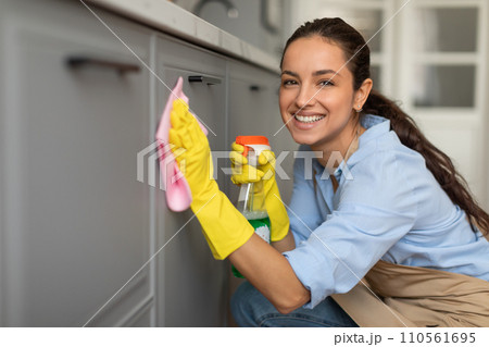Smiling caucasian woman in gloves cleaning cabinets with spray 110561695