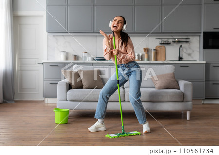 Woman singing into mop like a microphone, enjoying cleaning Woman singing into mop like a microphone, enjoying cleaning 110561734