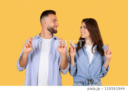 Couple crossing fingers for luck, hopeful expressions, yellow backdrop Couple crossing fingers for luck, hopeful expressions, yellow backdrop 110561944