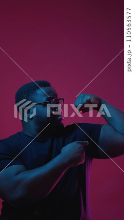 Showing power. Color light people. Strong confident man in glasses pointing at his biceps isolated on dark pink empty space background. 110563577