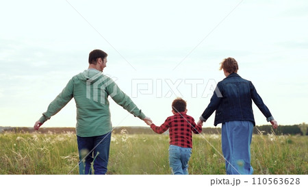 Parents and son energetically run holding each other hands across open field Parents and son energetically run holding each other hands across open field 110563628