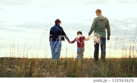 Happy family enjoys walk in field embracing joyous moments brought by wind Happy family enjoys walk in field embracing joyous moments brought by wind 110563629