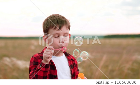 Happy boy finds happiness in blowing bubbles in field of cultivated plants 110563630